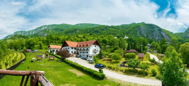Vila Sub Piatră, cu acoperișul de țiglă roșie, sub peretele calcaros al Bedeleului și schitul de pe deal